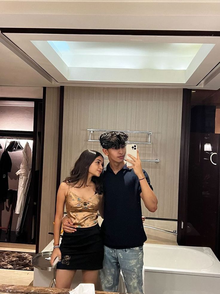 a man and woman standing in front of a mirror taking a selfie with their cell phone