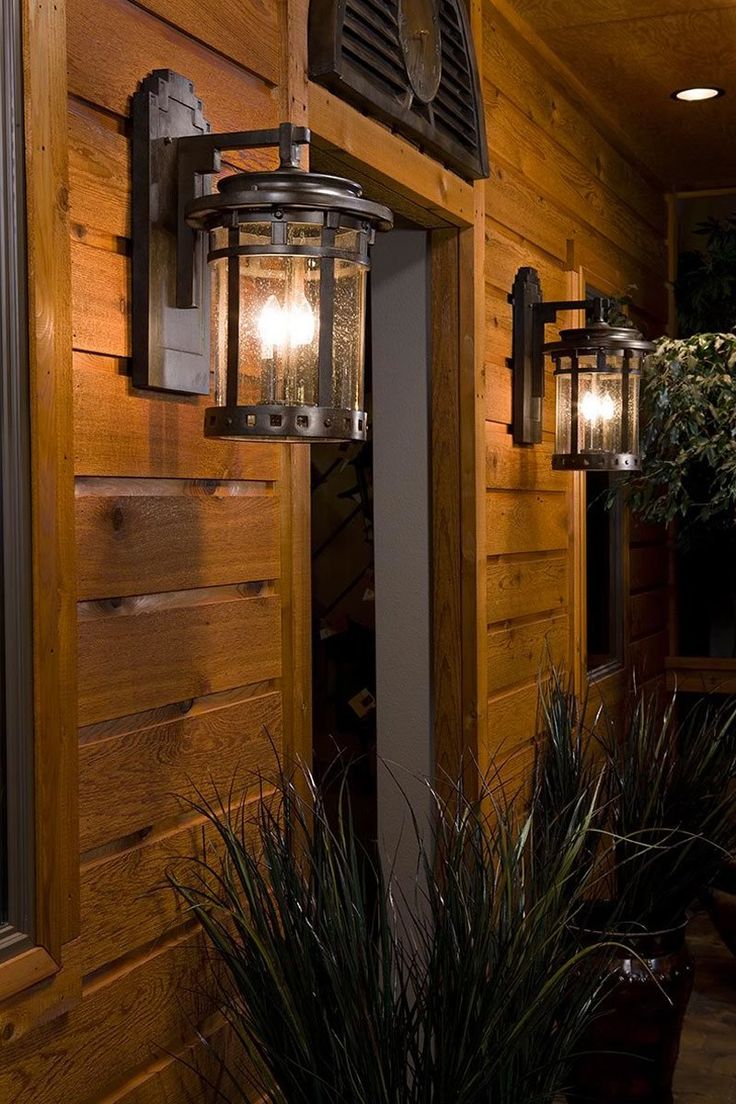 an outdoor light on the side of a wooden wall next to plants and potted plants