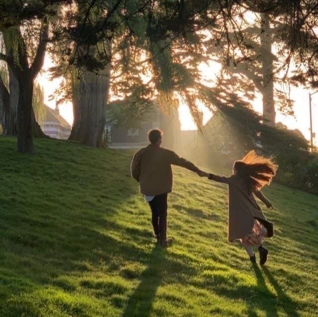 a man and woman holding hands walking across a lush green field