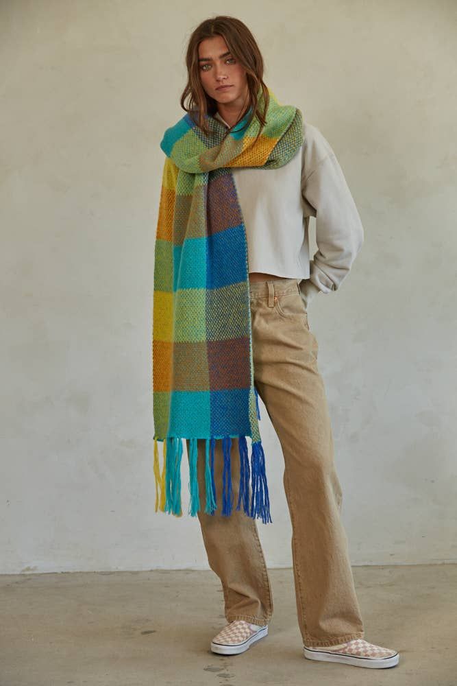 a woman standing in front of a white wall wearing a multicolored plaid scarf