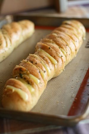 a long piece of bread with cheese and herbs on it sitting on a baking sheet