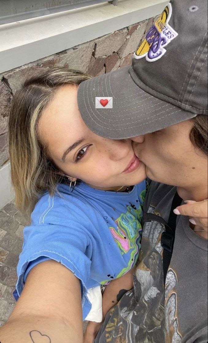 a man and woman taking a selfie in front of a brick wall with their arms around each other