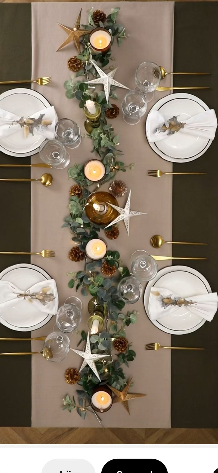 the table is set with white plates and silverware, gold candlesticks and greenery