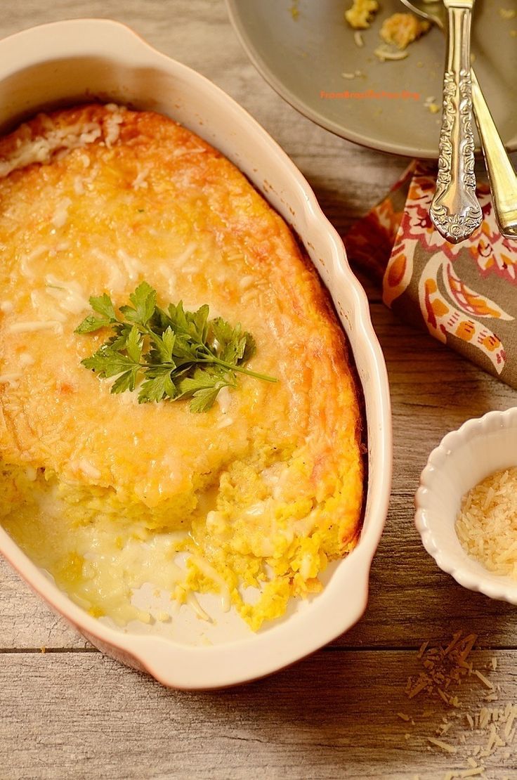 a casserole dish on a wooden table next to a plate and silverware