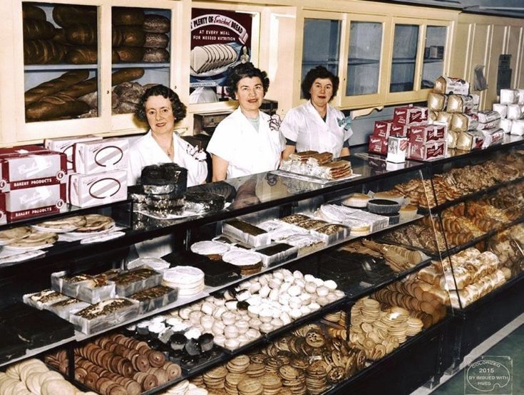 three people standing behind the counter of a bakery