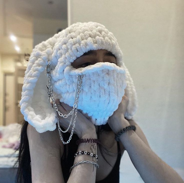 a woman covering her face with a crocheted hat and chain around her neck