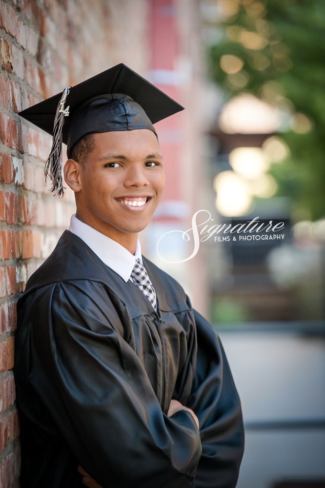 a young boy wearing a graduation cap and gown leaning against a brick wall with his arms crossed