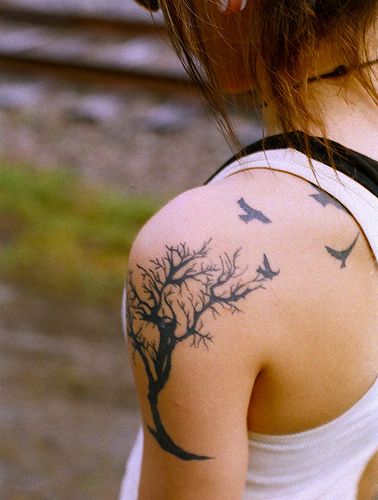 a woman with a tree and birds tattoo on her back shoulder is looking down at the ground