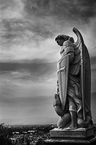 an angel statue on top of a hill with the city in the background and clouds overhead