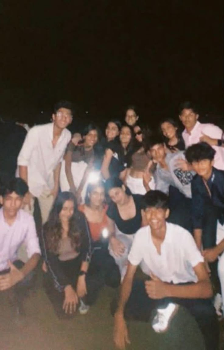 a group of young people posing for a photo together at night with their cell phones