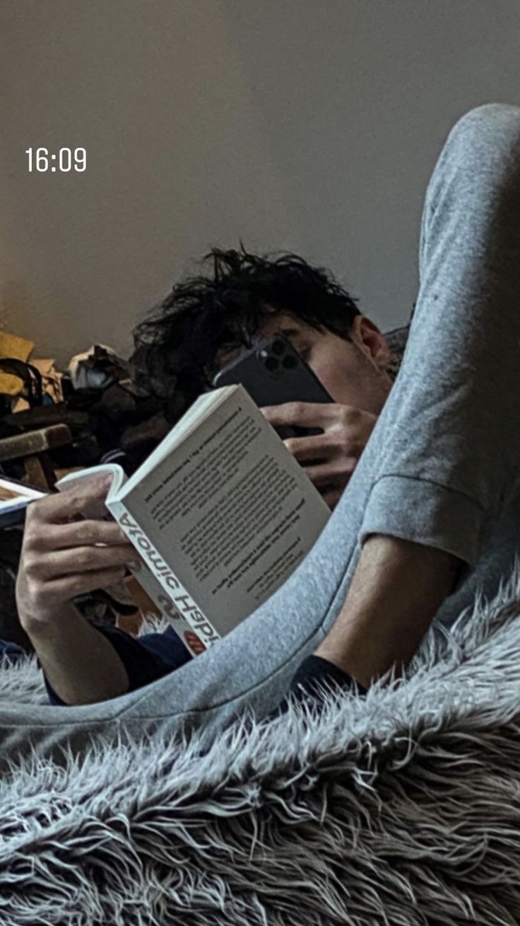 a man laying in bed reading a book