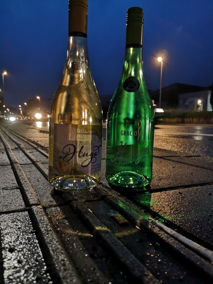 two bottles of wine sitting on the ground next to each other in front of some street lights