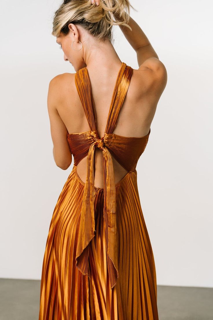 Stand out in our flattering Sandra Pleated Maxi Dress that comes in a Copper color. This dress will make you feel like a statement in any room! Party Dress With Bow Tie And Strappy Back, Satin Dress With Tie Back And Cross Back, Satin Cross-back Dress With Tie, Satin Cross-back Dress For Date Night, Satin Cross Back Dress For Date Night, Satin Party Dress With Cross Back, Chic Satin Cross Back Dress, Satin Cross Back Party Dress, Chic Satin Dress With Cross Back