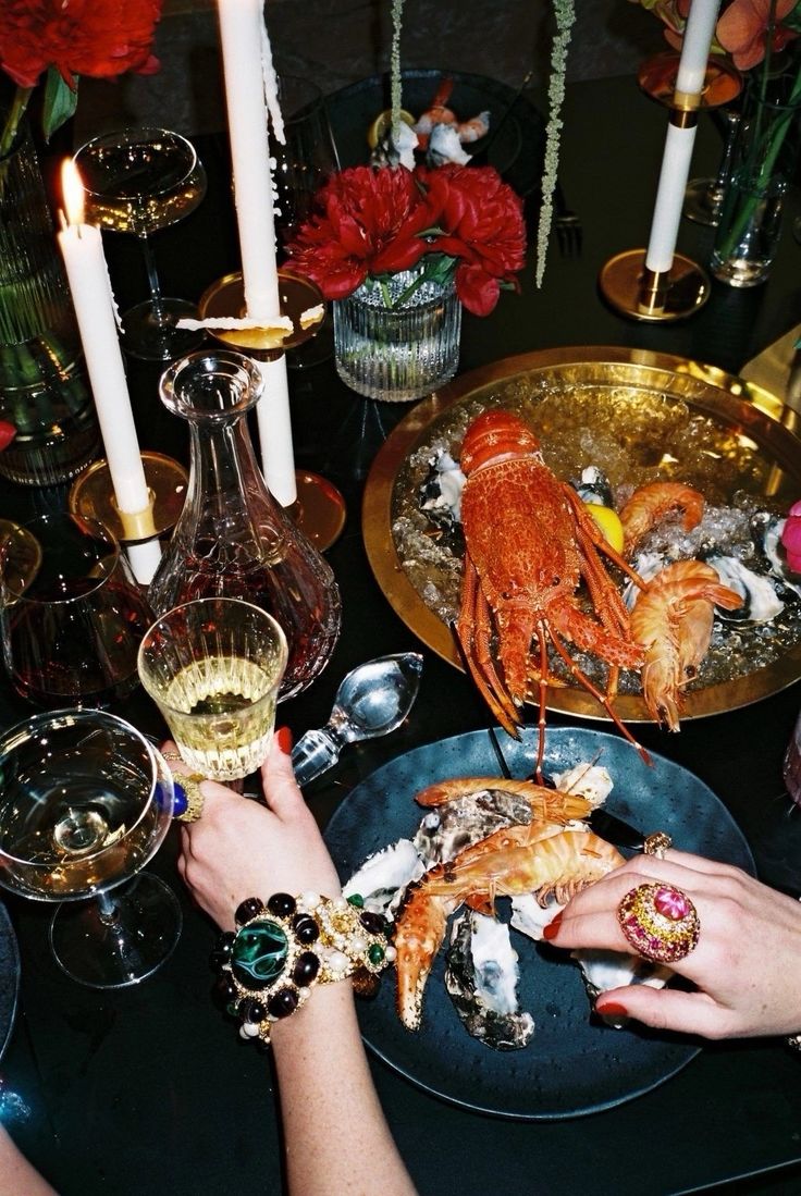 two people are eating lobsters at a table with candles and flowers in the background