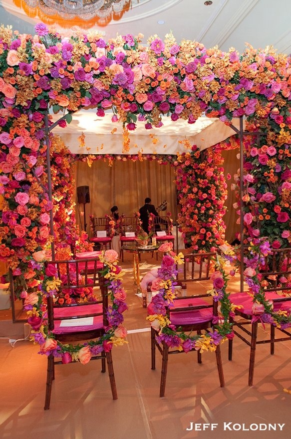 an outdoor wedding setup with pink and yellow flowers on the walls, purple chair covers, and white table cloths