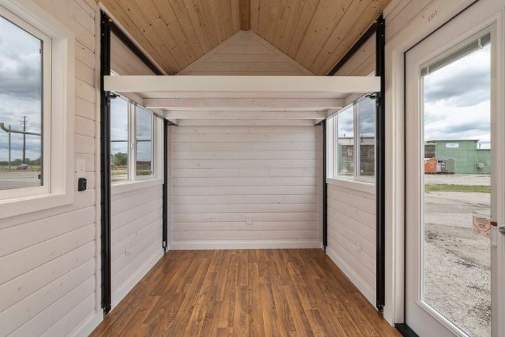 the inside of a tiny house with wood flooring and white walls, along with large windows