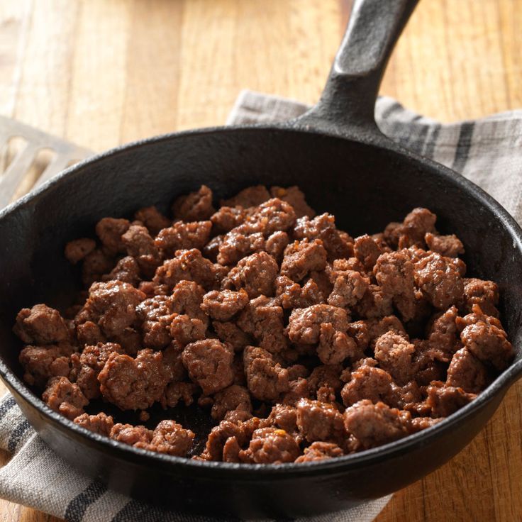 a pan filled with meat sitting on top of a wooden table next to a fork