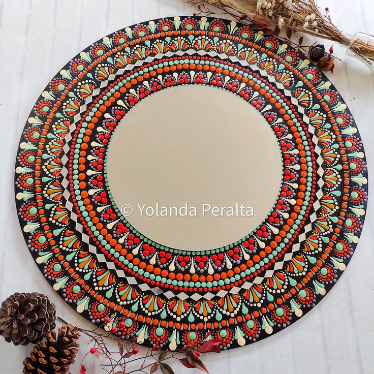 a round mirror sitting on top of a table next to pine cones and dried leaves