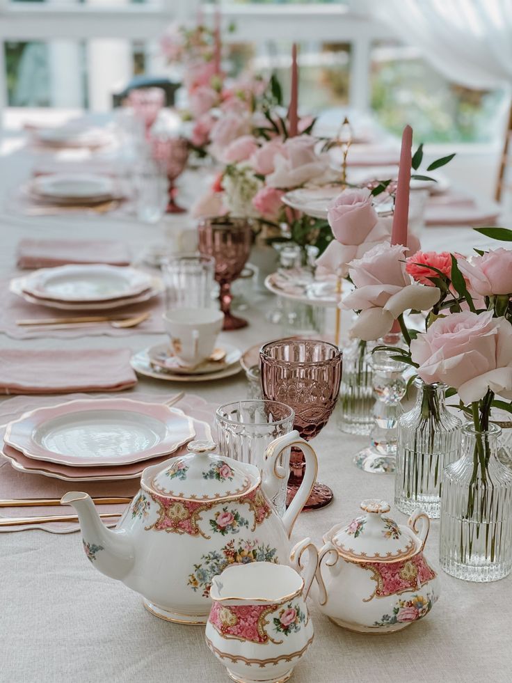 the table is set with pink roses and teapots, china dishes, and candles