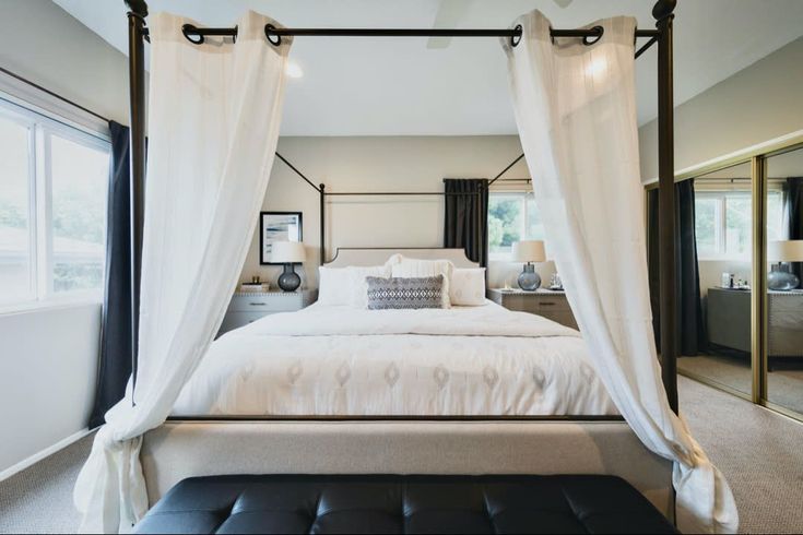 a bed with white drapes and pillows in a bedroom next to a large window