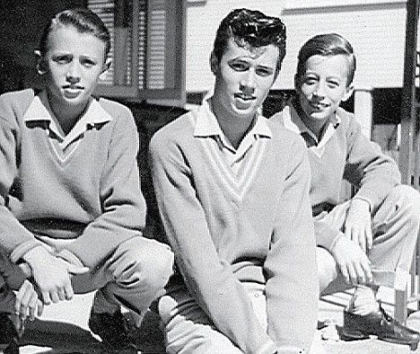 three young men sitting next to each other in front of a house and one man is wearing a polo shirt