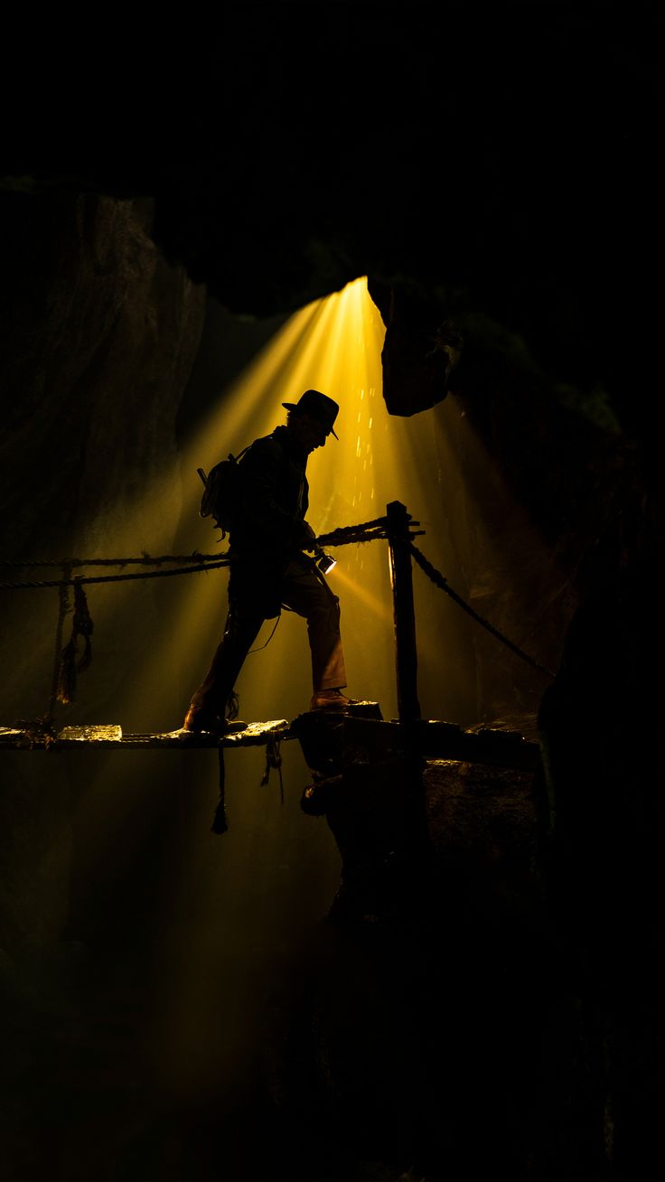 a man walking across a wooden bridge in the dark with light coming from behind him