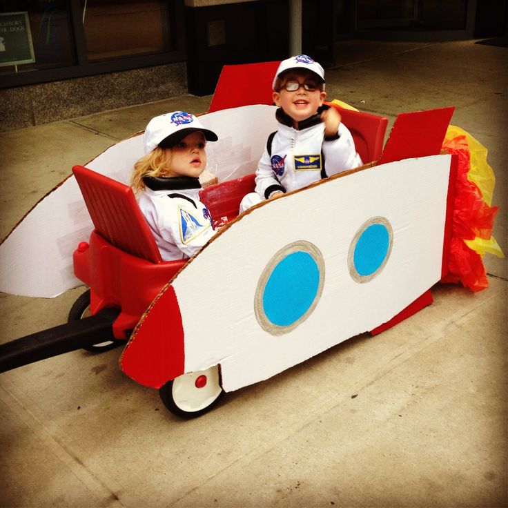 two children are sitting in a red and white boat shaped car that is made out of cardboard