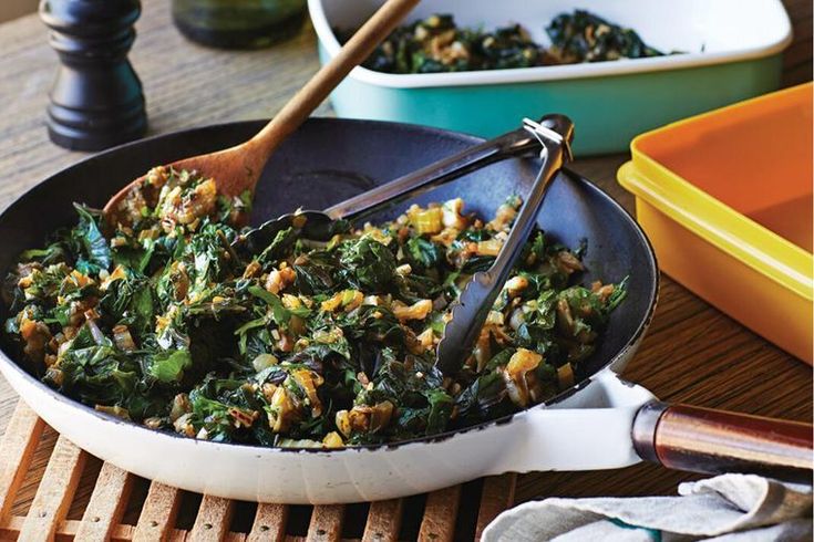 a pan filled with spinach and other food on top of a wooden table next to bowls