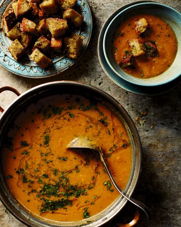 two bowls of soup and some bread on a table with utensils in them