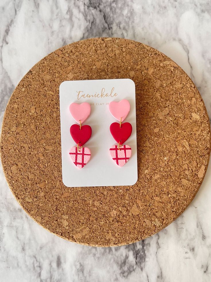 pink and red heart shaped earrings on top of a cork board next to a card