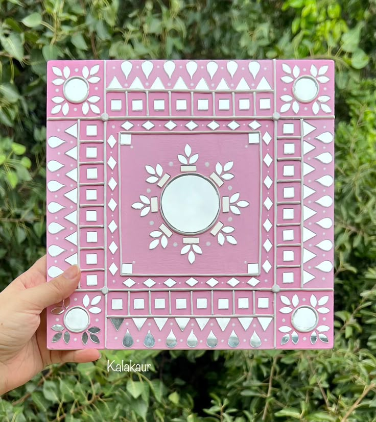 a hand holding up a pink and white box with an ornate design on the front