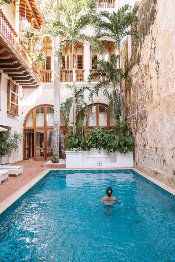 a person swimming in a large pool surrounded by palm trees and buildings with balconies on the second floor