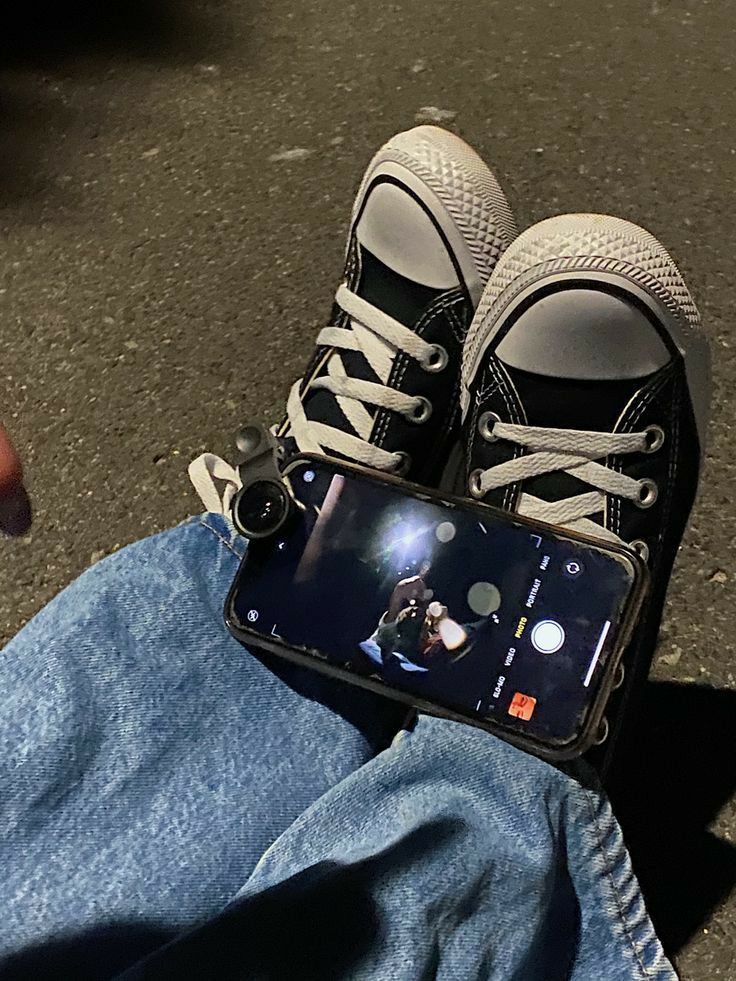 someone is holding their cell phone while sitting on the ground with his feet propped up