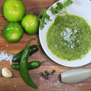 a white plate topped with green sauce next to peppers and other foods on a wooden table