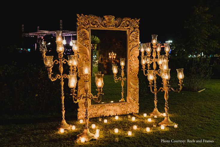 an elaborately decorated mirror and candles stand in the grass at night with lights on it