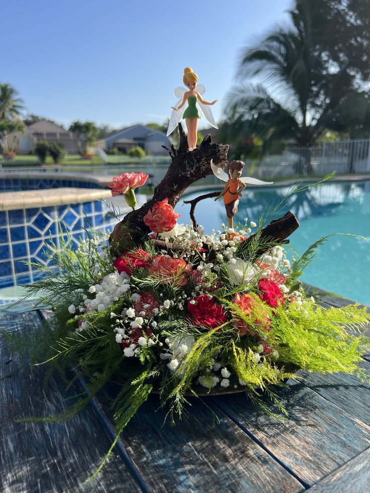 a flower arrangement sitting on top of a wooden table next to a pool