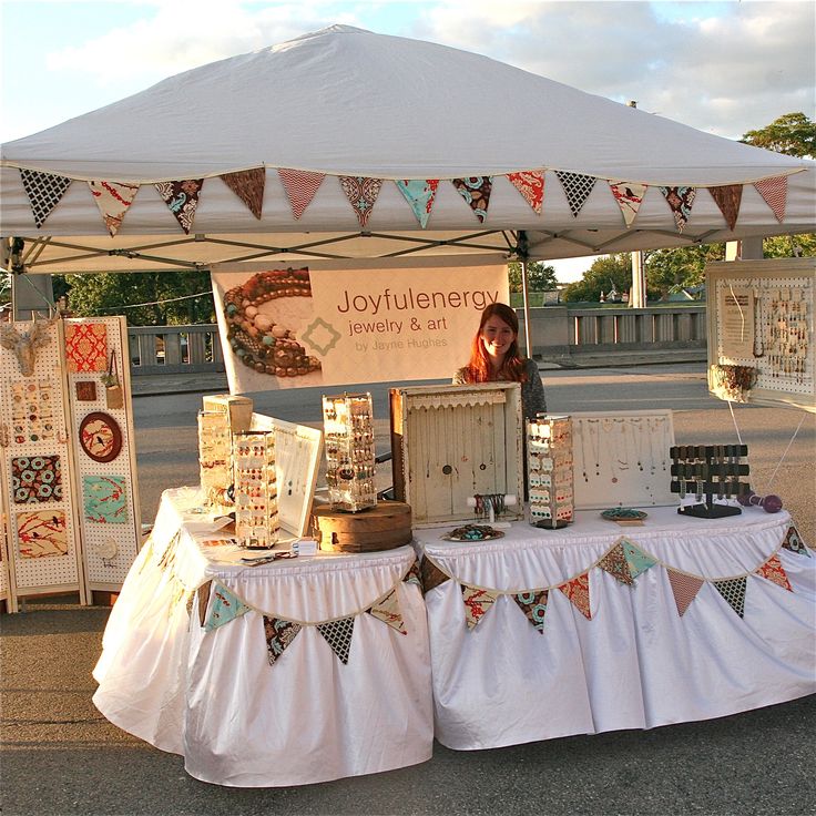 a woman standing behind a table with lots of items on it in front of a white tent