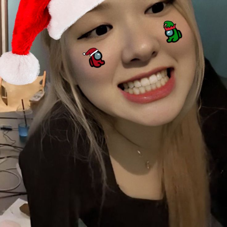 a girl wearing a santa hat with christmas stickers on her face and smiling at the camera