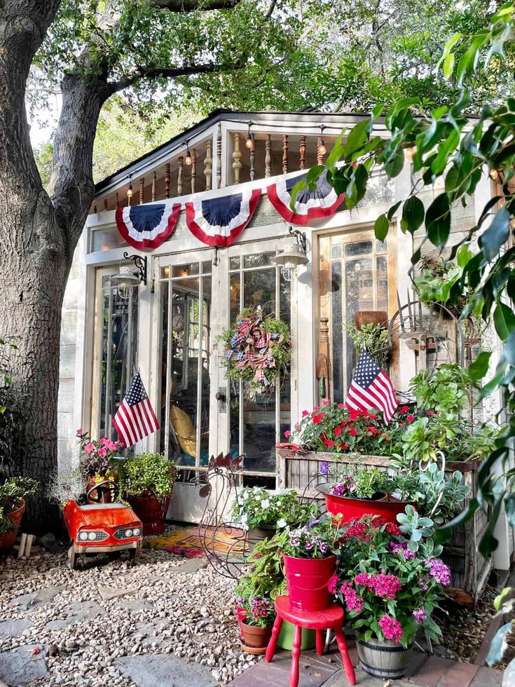 a small white house with american flags hanging from the roof and potted plants in front