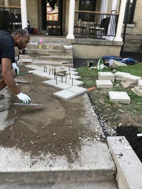 a man laying concrete on the ground in front of a house