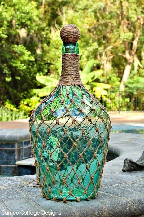 a green glass bottle sitting on top of a wooden table in front of some trees