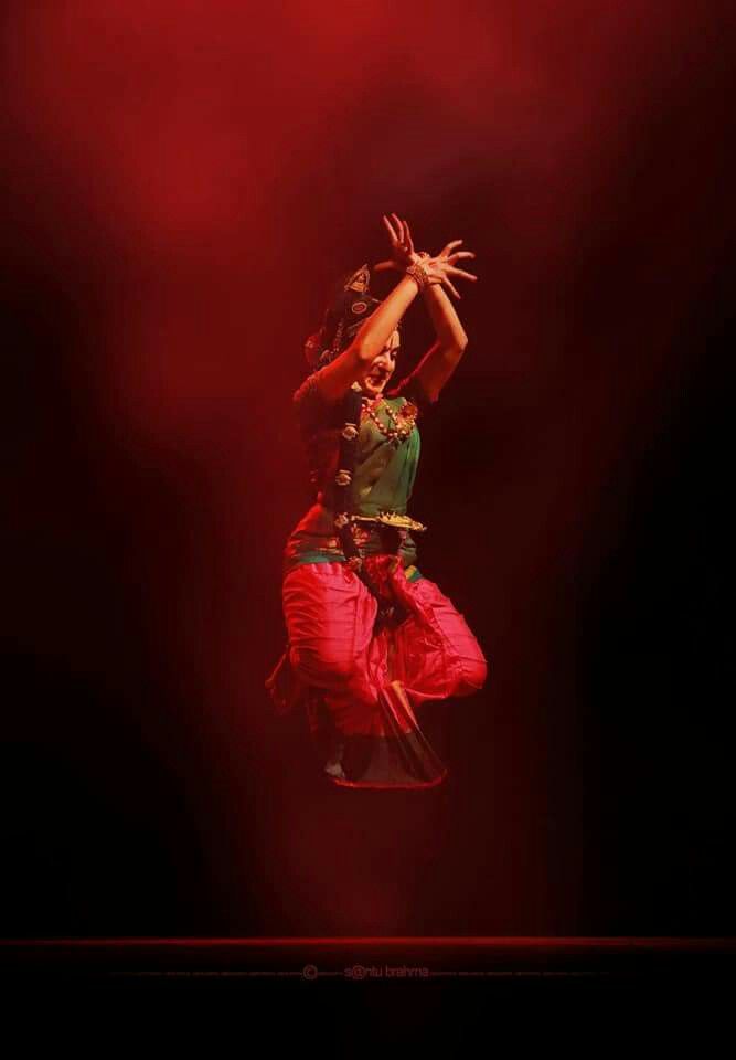 a woman is dancing on stage with her arms in the air while wearing red pants