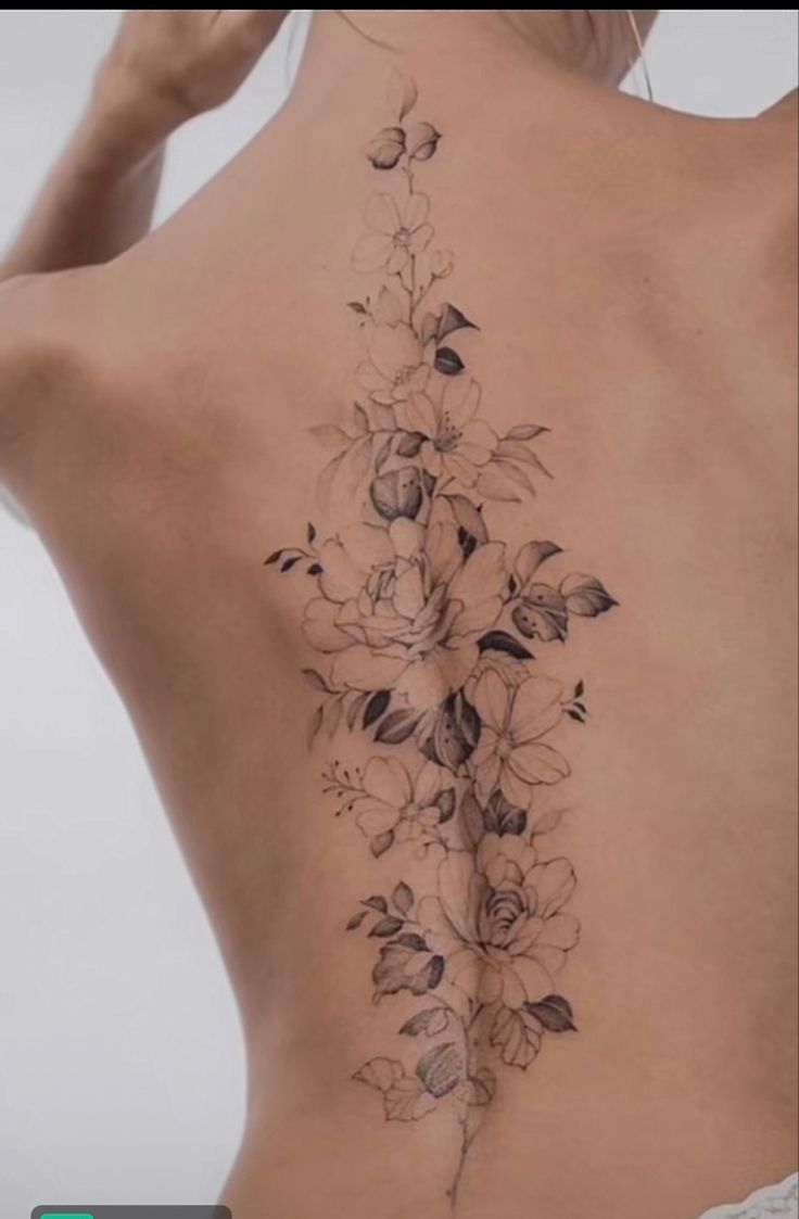 a woman's back tattoo with flowers and leaves on her left side ribcage