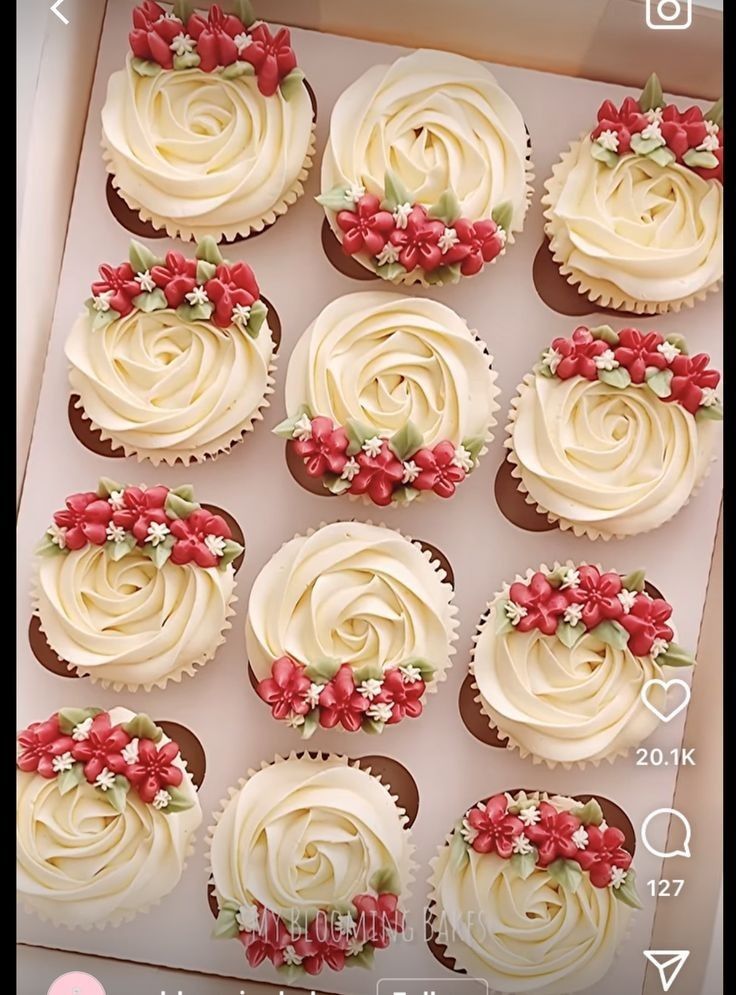 twelve cupcakes with white frosting and red flowers in a box on a table