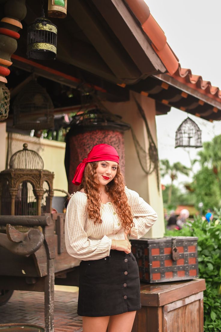 a woman wearing a red bandana standing in front of a birdcage with her hands on her hips