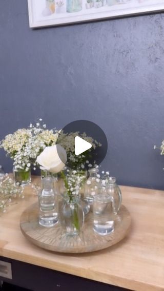 a wooden table topped with lots of vases filled with white flowers and greenery