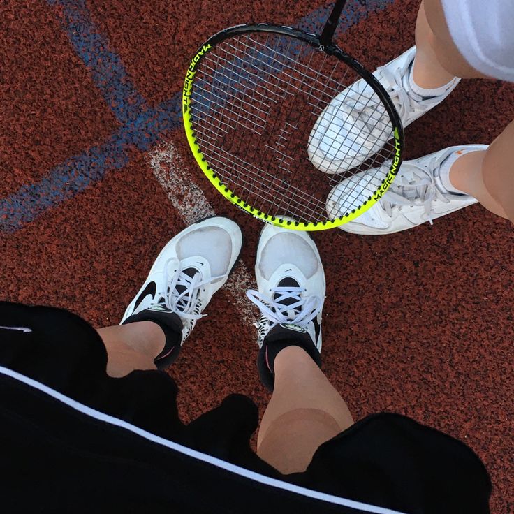 two people standing next to each other with tennis rackets in their hands on the ground