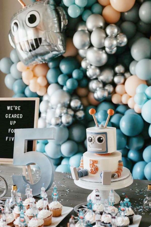 a table topped with cupcakes and cakes covered in frosting next to balloons