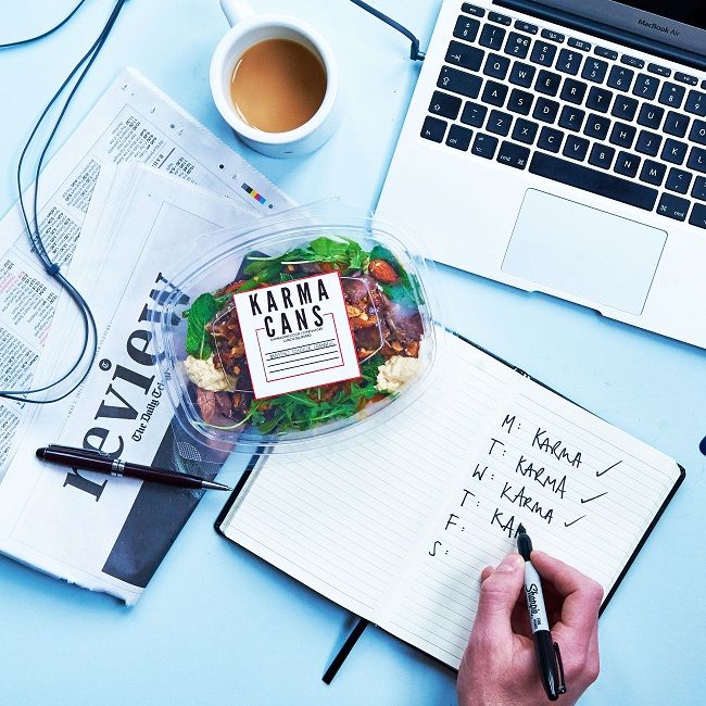 a person writing on a notepad next to a laptop and a salad in a plastic container