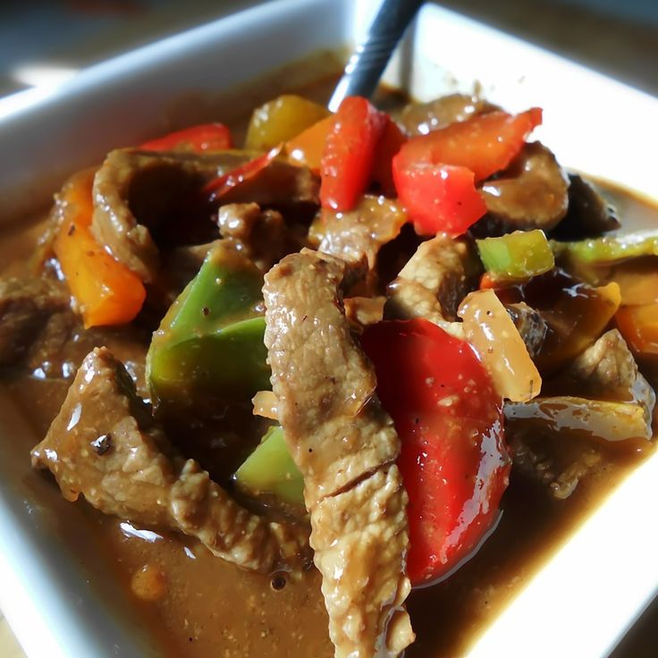 a white square bowl filled with meat and veggies on top of a table